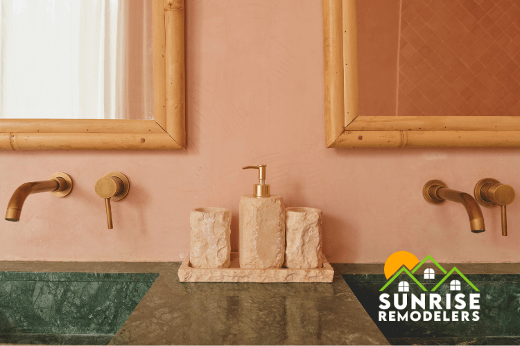 A rustic-modern bathroom featuring a double vanity with green marble countertops, wall-mounted bronze faucets, bamboo-framed mirrors, and soft pink walls. This unique design showcases the creative expertise of Sunrise Remodelers in bathroom remodeling and home renovation projects in Minnesota.